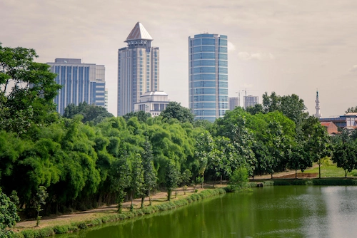Pemandangan taman dengan tanaman hijau dan danau di tengah perkotaan yang mengusung konsep kota hijau