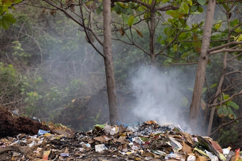 Tumpukan bekas pembakaran sampah yang mengeluarkan asap